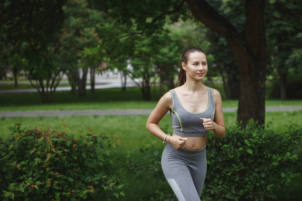 Νεαρή γυναίκα τρέξιμο μονοπάτι σε καταπράσινο πάρκο - Φωτογραφία, εικόνα