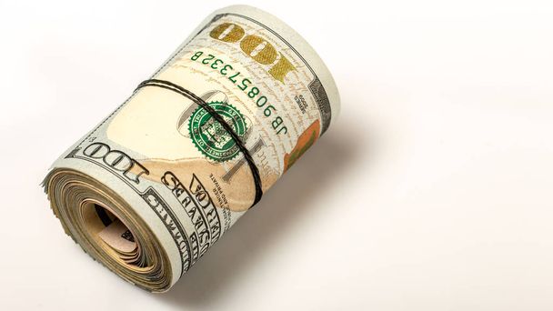 100 dollar bills twisted in buis en gebonden met een elastische band. witte achtergrond. Close-up - Foto, afbeelding