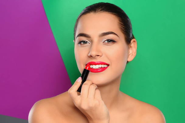 Young woman applying lipstick on color background - Фото, изображение