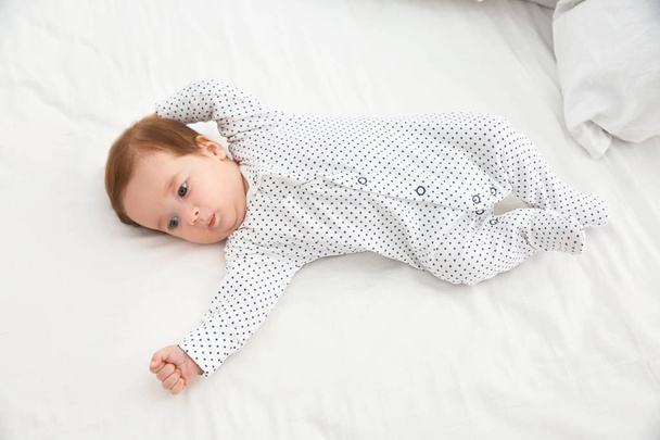 Adorable baby in cute footie on white sheet, above view - Foto, immagini