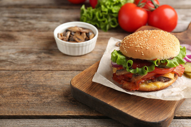 Tasty burger with bacon on wooden board. Space for text - Foto, afbeelding