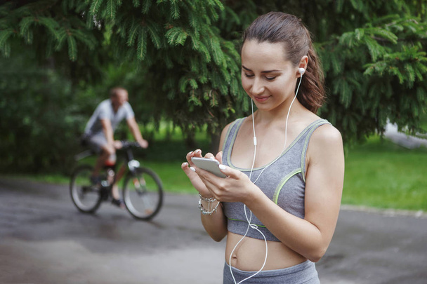 緑豊かな公園の道をジョギングしながら音楽を聴いてかわいい若い女性 - 写真・画像