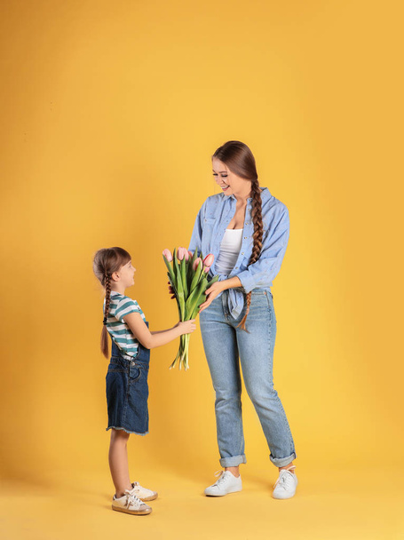 Happy mother and daughter with flower bouquet on color background. International Women's Day - Foto, imagen