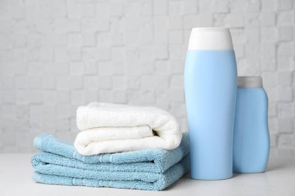 Folded towels and shampoo on table against white wall - Photo, image