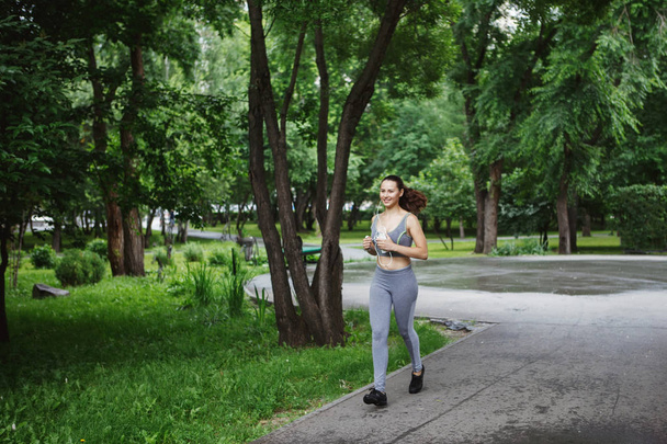 Young woman jogging down path in green park - Zdjęcie, obraz