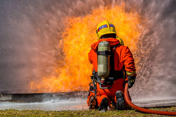 Feuerwehrmann mit Feuerlöscher und Wasser aus Schlauch zur Brandbekämpfung, Feuerwehrmann, der Hochdruckwasser versprüht, um Feuer mit Kopierraum zu machen. - Foto, Bild