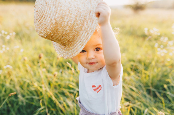 小さな赤ちゃん女の子麦藁帽子を保持していると日没に夏の田舎に歩いて - 写真・画像