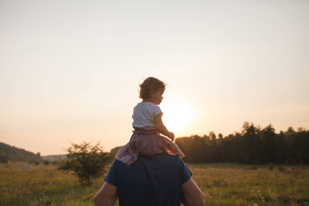 Νεαρός πατέρας δαπάνες χρόνο με βρέφος την κόρη στην ύπαιθρο στο ηλιοβασίλεμα   - Φωτογραφία, εικόνα