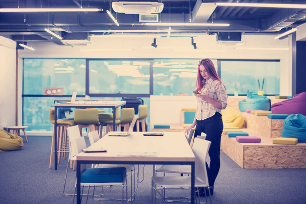 young redhead businesswoman reading a text message on her mobile phone while having a break in the modern startup office - Photo, image