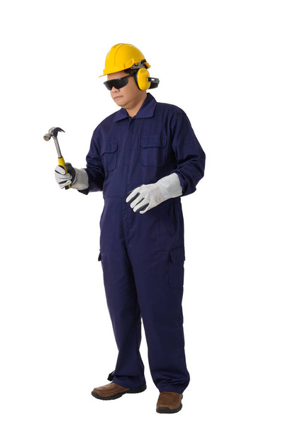Γεμάτο σώμα πορτρέτο ενός εργαζομένου σε μηχανικό Jumpsuit κρατάει ένα σφυρί με κράνος, ωτοασπίδες, προστατευτικά γάντια και προστατευτικά δίοπτρα ασφάλειας που απομονώνονται σε λευκό φόντο διαδρομή αποκοπής - Φωτογραφία, εικόνα