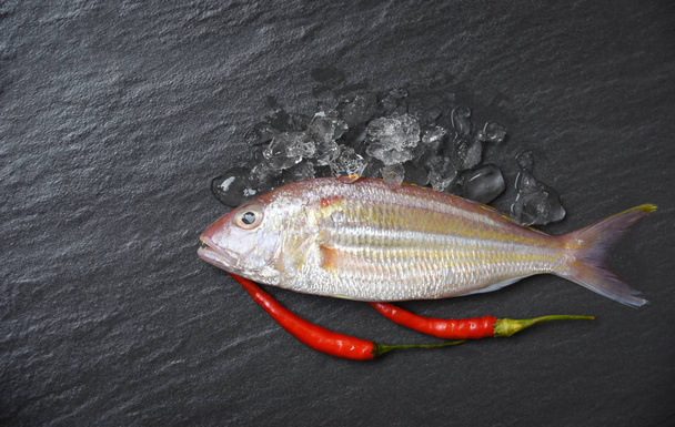 Φρέσκο ωμό ψάρι σε σκούρο φόντο πάγου / θαλασσινά ψάρια ωκεανού γκουρμέ για μάγειρα με κόκκινο τσίλι στο εστιατόριο - Φωτογραφία, εικόνα