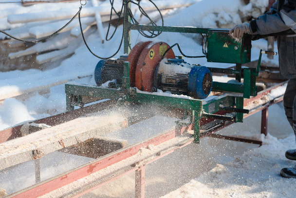 Sawing boards on the sawmill. Cook lumber in winter. Work on the sawmill. Sawing boards in winter. - Foto, Imagen