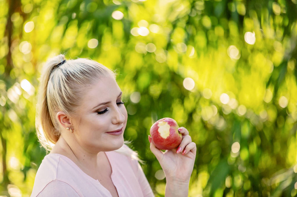 Healthy young female thinking about her diet while eating an apple against a bright sunlit background - Photo, Image