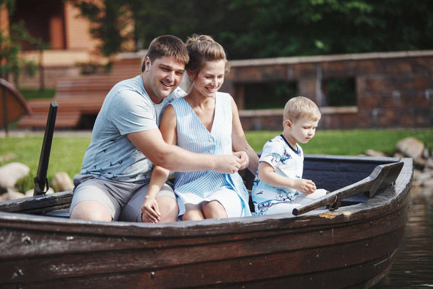 Mother, father and son sitting in wooden boat with oars and feeding fish with bread - Photo, Image
