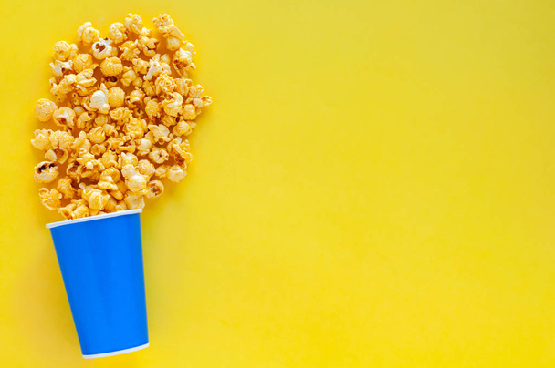 süßes Karamell-Popcorn in blauem Papiereimer isoliert auf gelbem Hintergrund mit Platz für Text. - Foto, Bild