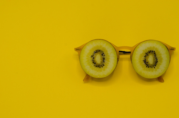 İki dilim altın kivi meyve üzerinde sarı güneş gözlüğü koymak metin için yer için yaz saati Sarı zemin üzerine izole gözleri fotoğraf ile yüzü olarak ayarla. - Fotoğraf, Görsel