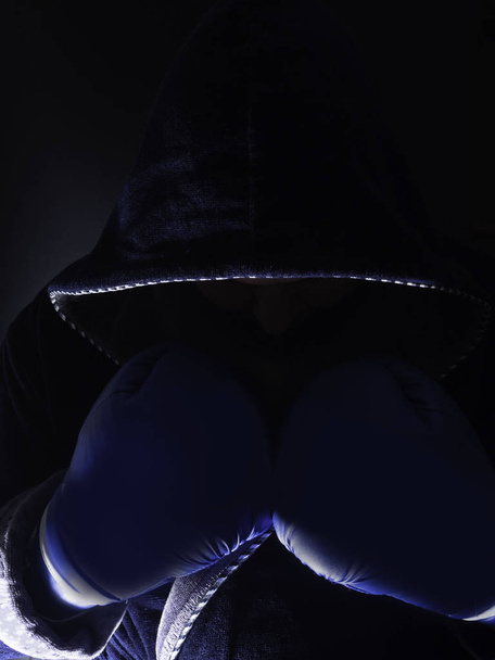 boxeador con capucha usando guantes de boxeo posando en la oscuridad, listo para boxear
 - Foto, imagen