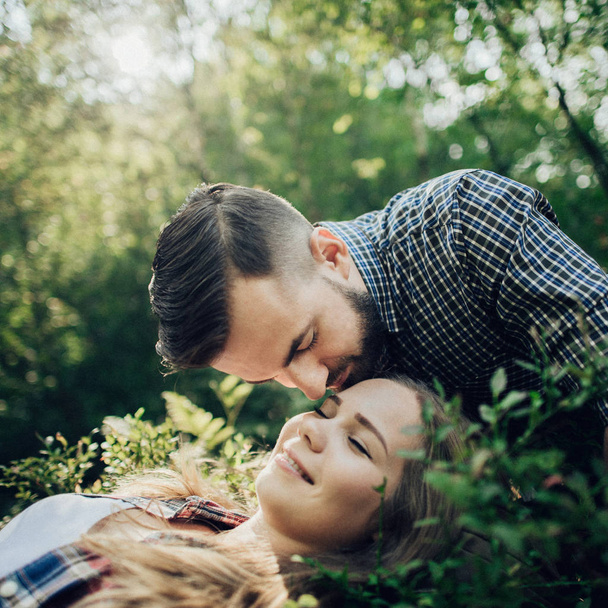 Young woman lying on green leaves and man kissing forehead  - Foto, afbeelding