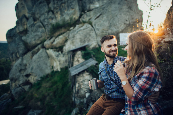 Young couple drinking hot tea at sunset in mountains - Фото, изображение
