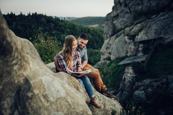 Young couple reading book on mountain edge  - Photo, image