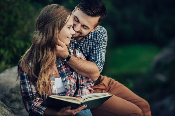 Young couple sitting on rock and reading book - Фото, зображення