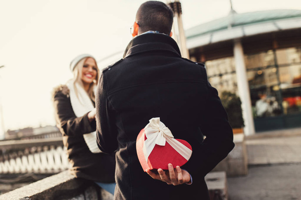 A fiatal gyönyörű pár élvezi a városi sétát Valentin-napon. A barátja ajándékot ad a barátnőjének.. - Fotó, kép