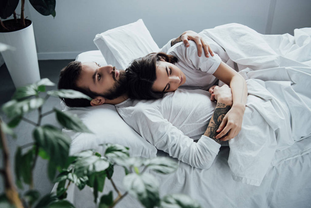 beautiful young couple in pajamas embracing while lying in bed at home - Photo, Image