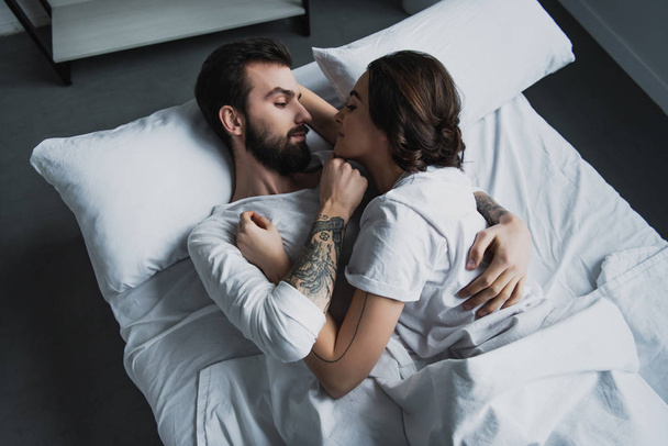 vonzó fiatal pár pizsamában átfogó fekve az ágyban otthon - Fotó, kép