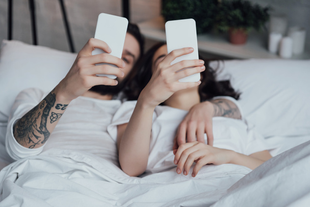 νεαρό ζευγάρι ξαπλωμένη στο κρεβάτι και χρησιμοποιώντας τα smartphones  - Φωτογραφία, εικόνα