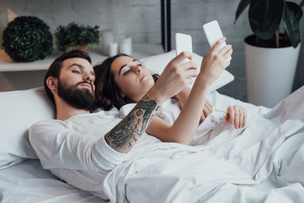 красива молода пара лежить в ліжку і використовує смартфони
  - Фото, зображення