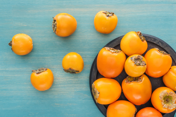top view of orange ripe persimmons on black plate  - Zdjęcie, obraz