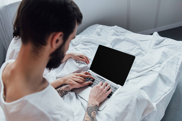 back view of couple holding hands and using laptop with blank screen at home in bed - Foto, imagen