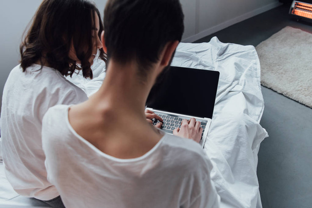 visão traseira do casal deitado na cama e usando laptop com tela em branco
  - Foto, Imagem