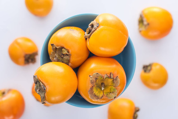 selective focus of ripe persimmons on blue glass plate - Fotoğraf, Görsel