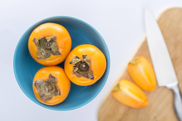 selective focus of persimmons on blue glass plate and slices on cutting board  - Photo, Image