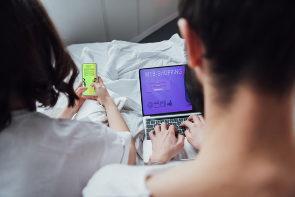 Widok z para leży w łóżku i korzystania z urządzeń cyfrowych z zakupy online na ekranie z tyłu  - Zdjęcie, obraz