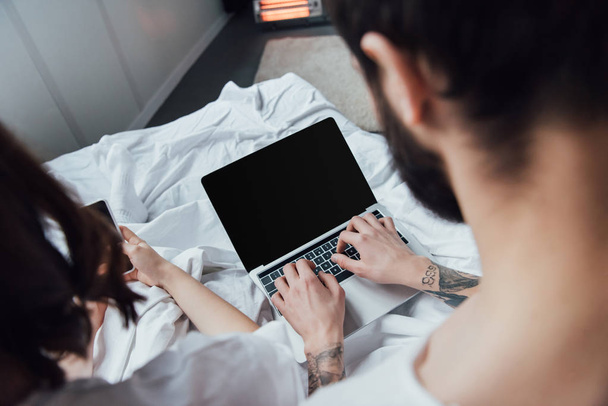 back view of couple lying in bed and using laptop with blank screen at home - Fotoğraf, Görsel
