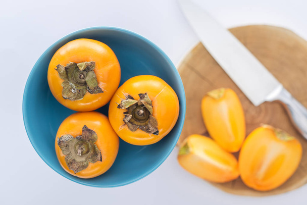 selective focus of persimmons on blue plate and slices on cutting board  - Photo, Image