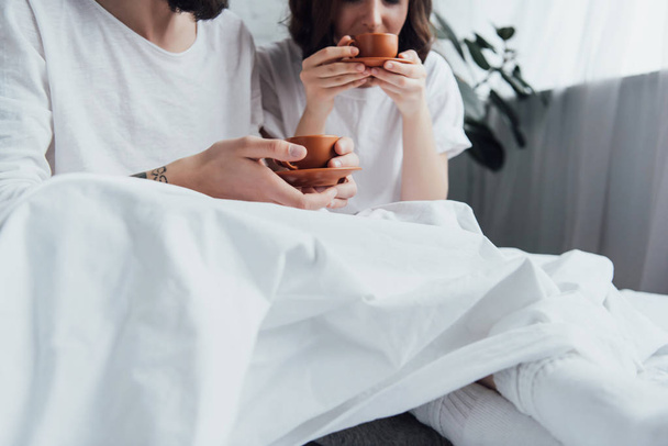 μερική άποψη του νεαρό ζευγάρι ξαπλωμένη στο κρεβάτι και πίνοντας τον καφέ πρωί - Φωτογραφία, εικόνα