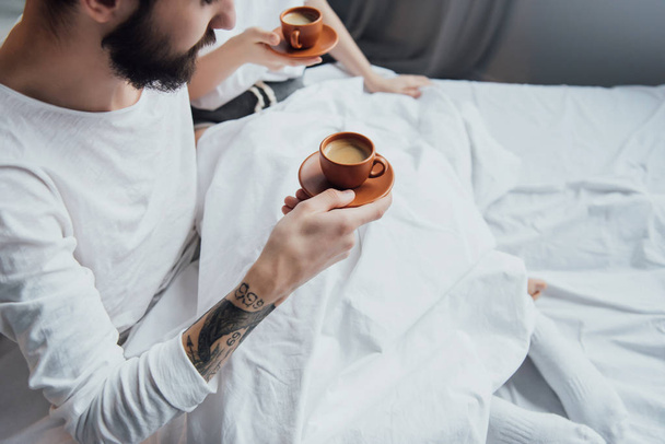 częściowy widok Młoda para z filiżanki kawy w łóżku z miejsca kopii - Zdjęcie, obraz