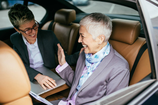 Senior mujer de negocios y su asistente sentado en la limusina hablando y trabajando
. - Foto, Imagen