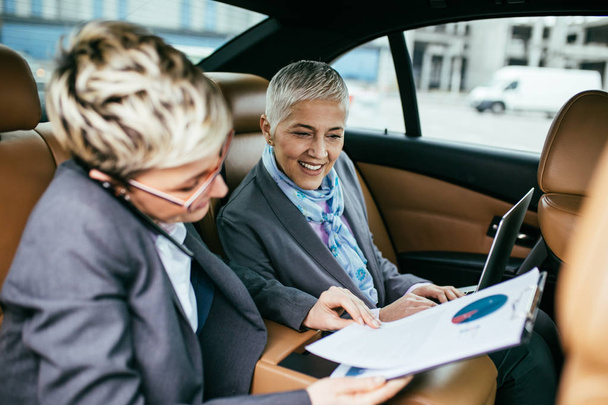 Senior mujer de negocios y su asistente sentado en la limusina hablando y trabajando
. - Foto, Imagen