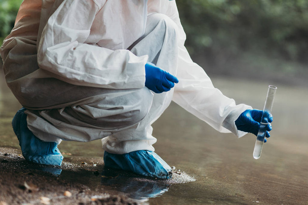 Ученый в защитном комплексе берет пробы воды из реки - Фото, изображение