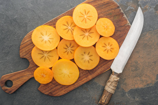 vista superior de cáqui de laranja fatiado na placa de corte com faca
  - Foto, Imagem