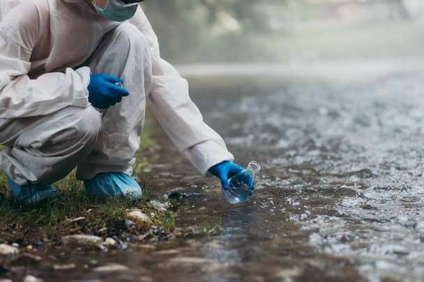 Naukowiec w ochronnym apartamencie pobierający próbki wody z rzeki - Zdjęcie, obraz