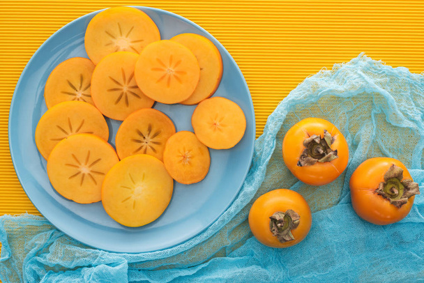 top view of orange persimmons slices on blue plate - Foto, imagen
