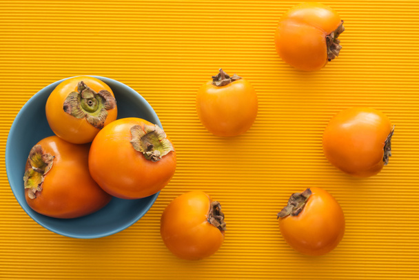 top view of orange persimmons on blue plate on yellow background  - 写真・画像