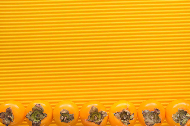 Draufsicht auf ganze orangefarbene Persimmons auf gelbem Hintergrund mit Kopierraum - Foto, Bild