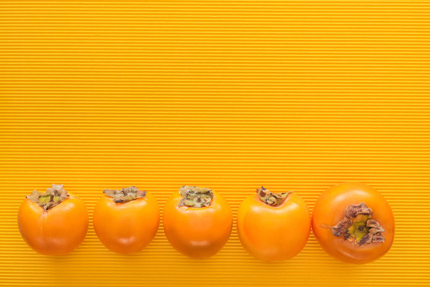 top view of orange persimmons on yellow background  with copy space - Φωτογραφία, εικόνα