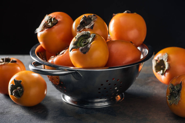 orange and ripe persimmons in colander isolated on black - Fotoğraf, Görsel